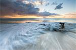 The waves and caribbean sunset frames tree trunks on Ffryers Beach Antigua and Barbuda Leeward Islands West Indies