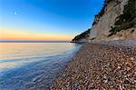 The moon rises during sunset at Faraglioni Beach (Baia delle Zagare), Mattinata, Apulia (Puglia), Italy.