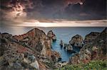 Hiker on top of cliffs surrounded by the ocean under the cloudy sky at sunrise Ponta Da Piedade Lagos Algarve Portugal Europe