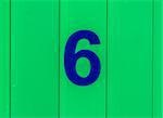the number six, blue, set against bright green wood