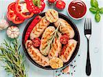 Top view of chicken homemade sausages, sauces ketchup and vegetables and herbs on blue wooden background. Grilled sausages and grilled vegetables in black iron pan. Top view or flat lay.