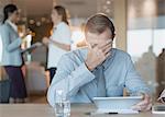 Tired, stressed businessman using digital tablet in conference room