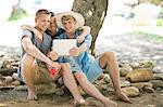Three young male friends sitting on rocks looking at digital tablet