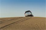 Off road vehicle driving over top of desert dunes, Dubai, United Arab Emirates