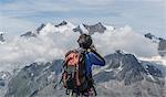 Rear view of male climber photographing low mountain clouds at Jegihorn, Valais, Switzerland