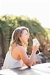 Young woman sitting outdoors, drinking from wine glass, smiling