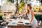 Young woman, outdoors, preparing dinner table, pouring wine