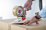 Cropped view of man sealing cardboard box with parcel tape