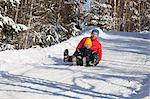 Man and son tobogganing in snow covered forest