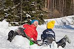 Man and son laughing after falling from toboggan in snow covered landscape