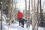 Man and son looking up while walking through snow covered forest