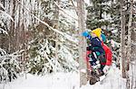 Man helping son climb tree in snow covered forest