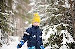 Portrait of boy in yellow knit hat walking in snow covered forest
