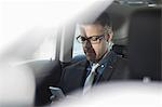 Businessman sitting in back of car, holding smartphone
