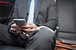 Businessman sitting in back of car, using smartphone, mid section