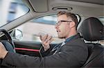 Businessman driving car, speaking into smartphone