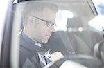 Businessman in car, putting on seatbelt, view through car window