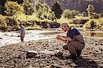 Young fisherman crouching with fishing rod by river, Mozirje, Brezovica, Slovenia