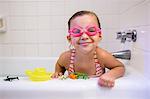 Portrait of girl wearing swimming goggles in bath, looking at camera smiling
