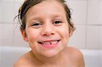 Portrait of girl with missing tooth in bath, looking at camera smiling