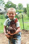 Boy holding speckled hen looking at camera smiling