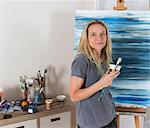 Portrait of mature female artist with abstract canvas  in studio