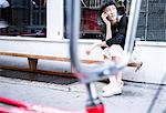 Young stylish woman sitting outside shop making smartphone call