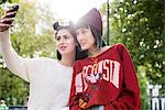 Two young stylish women taking smartphone selfie in city park