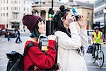 Two young stylish women taking photographs on street, London, UK