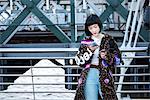 Stylish young woman looking at smartphone on millennium footbridge, London, UK