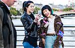 Two young stylish women laughing at smartphone on millennium footbridge, London, UK