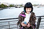 Stylish young woman looking at smartphone on millennium footbridge, London, UK