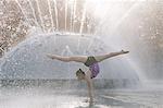 Teenage girl beside fountain, balancing on hands in yoga position