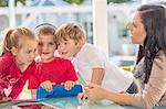 Mid adult woman sitting with three young children, young boy holding digital tablet, wearing headphones