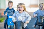 Girl and boys at preschool, racing push motorbikes in garden