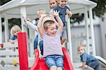 Boys and girls at preschool, sliding on playground slide in garden