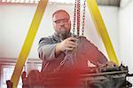 Male car mechanic attaching hoist chain to car engine in repair garage