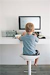 Rear view of boy at desk typing on computer