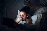 Girl in bed blowing nose, illuminated by light from digital tablet