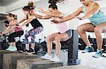 Determined women doing jump squats on boxes in exercise class