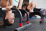 Focused young woman doing upside-down shoulder stand with equipment at gym