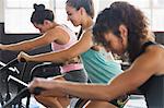 Focused young women using elliptical bikes in exercise class