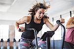 Determined young woman riding elliptical bike in gym