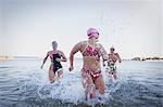 Female open water swimmers running, splashing in ocean surf