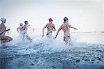 Female open water swimmers running and splashing in ocean surf