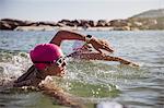 Determined female open water swimmer with smart watch swimming in sunny ocean