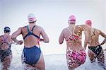 Female open water swimmers running and splashing in ocean surf