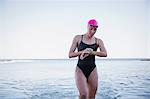 Female open water swimmer checking time on smart watch in ocean surf