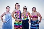 Portrait confident, smiling female open water swimmers wrapped in towels