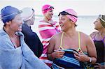 Female open water swimmers talking and drying off with towels on beach